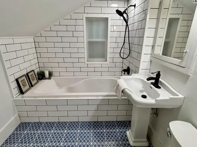 This bathroom features white subway tile, a pedestal sink, and a patterned tile floor.