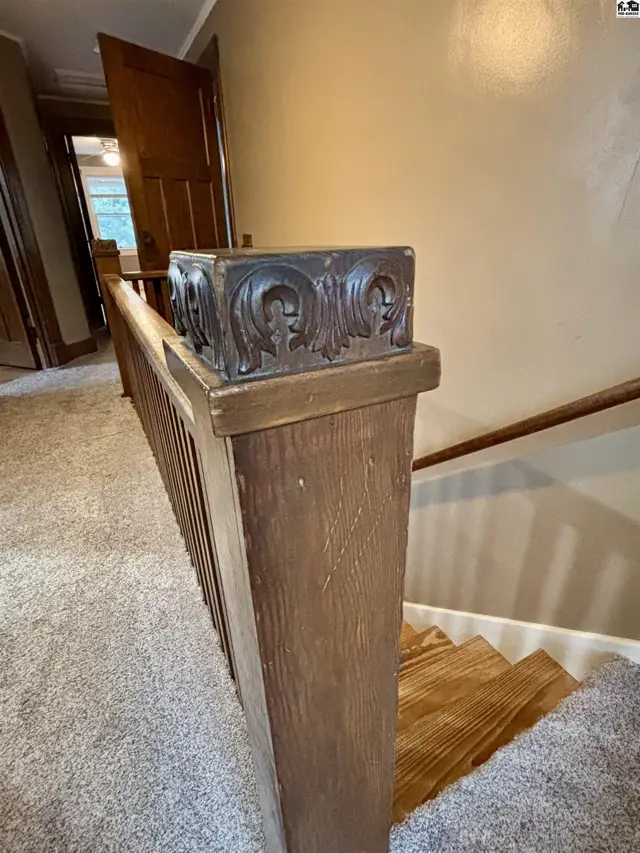 Wooden banister with carved detail ascends carpeted stairs with wooden treads.