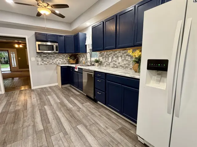 This kitchen features navy blue cabinets, a stainless steel dishwasher, and a white refrigerator.