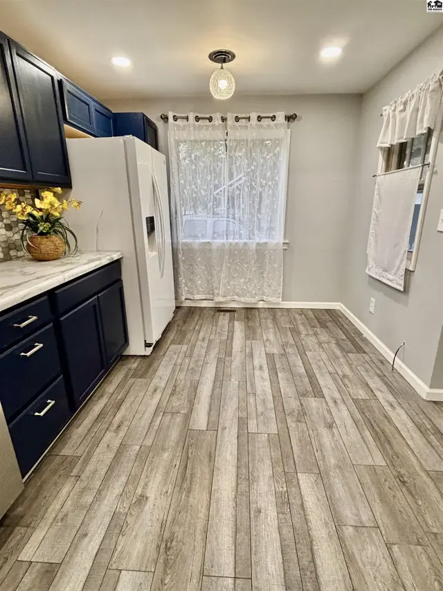 This kitchen features dark blue cabinets, white countertops, and wood-look flooring.