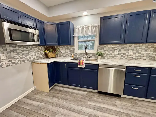 This kitchen features dark blue cabinets, a stainless steel dishwasher, and a mosaic tile backsplash.