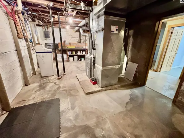 Concrete floors and walls feature exposed pipes, ductwork, and a water heater.
