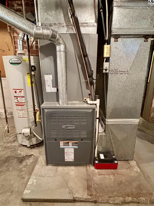 A gas furnace, water heater, and metal ductwork are installed on a concrete floor.
