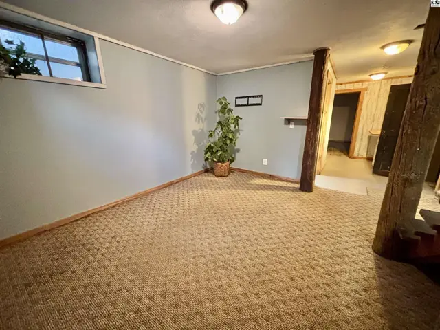 Carpeted room with light blue walls, a small window, and exposed wooden beams.