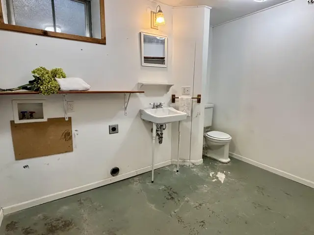 This room features a sink, toilet, and laundry hookups with a wooden shelf.