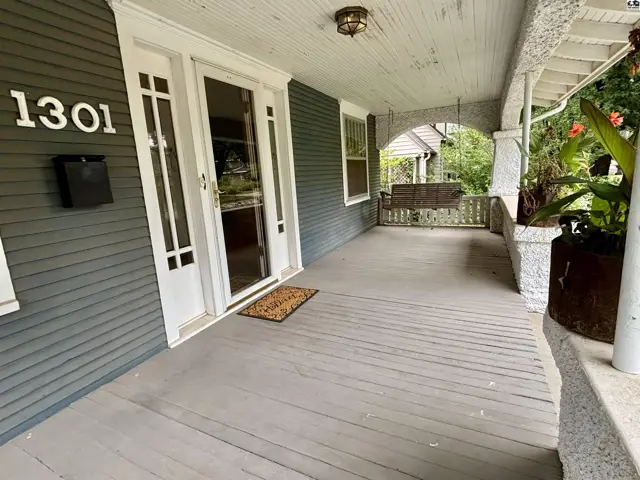 Covered front porch with wood flooring, swing, and stone columns.