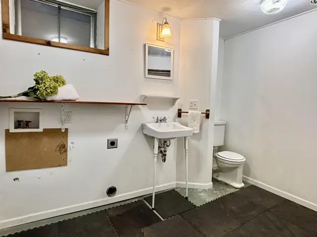 This room features a toilet, sink, and laundry hookups with a wooden shelf.