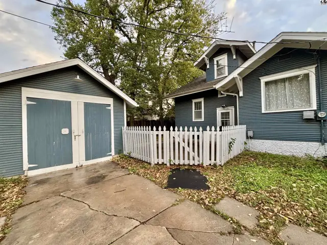 A detached garage with double doors sits beside a home with white picket fencing.