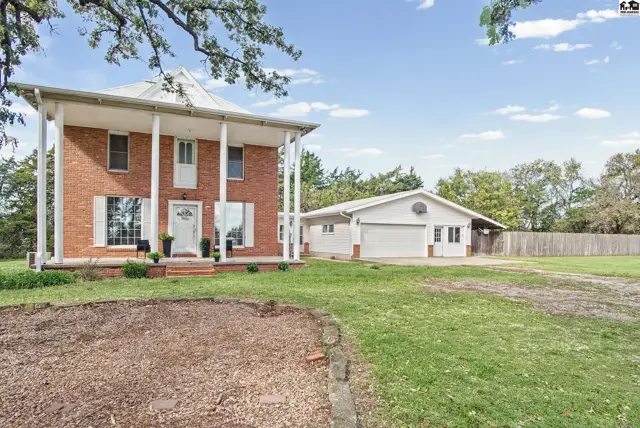 Brick home with a covered porch, attached garage, and mature trees.