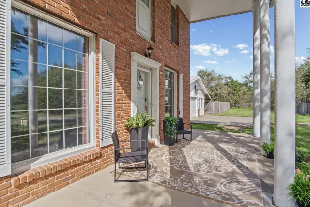 Covered front porch with brick exterior, white columns, and a patterned rug.