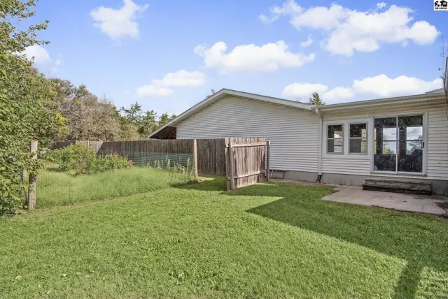 A wooden fence encloses a grassy yard with a concrete patio.