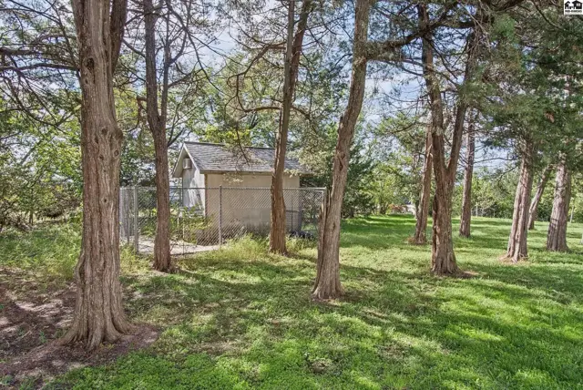 A small, concrete building with a chain-link fence sits among mature trees.
