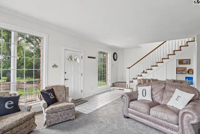 Spacious living area with large windows, a staircase, and neutral carpeting.