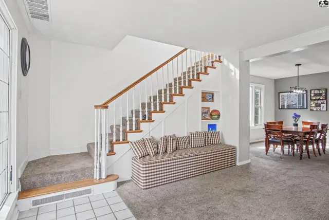 Carpeted stairs with white spindles lead to a landing, adjacent to a built-in bench.