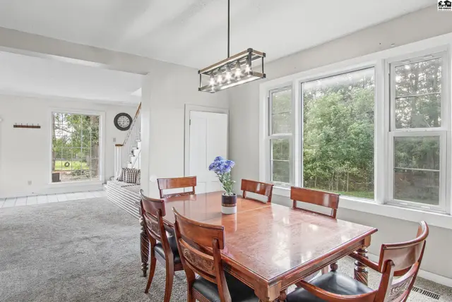 Spacious dining room with a large wooden table and six chairs, featuring a modern chandelier.
