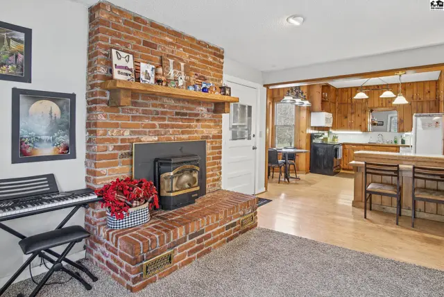 Brick fireplace with wood stove insert anchors the living area adjacent to a wood-paneled kitchen.