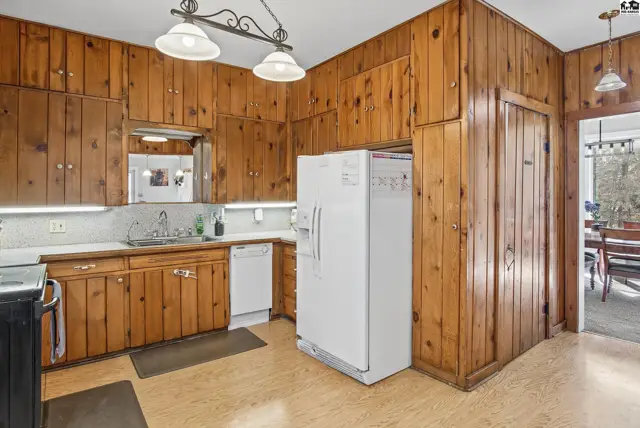 Wood-paneled walls surround a kitchen with white appliances and countertops.