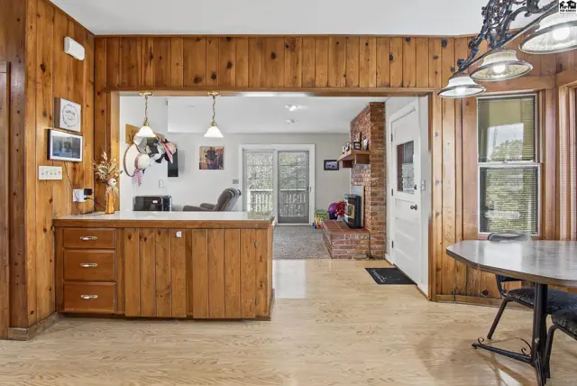 Wood-paneled walls and cabinets frame a view into a living area with a brick fireplace.