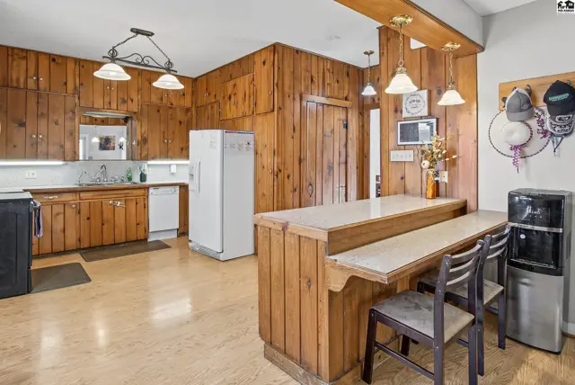 Wood-paneled kitchen features a breakfast bar, white appliances, and ample cabinet space.