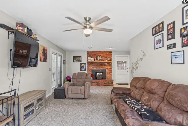 Spacious living room features a brick fireplace, ceiling fan, and plush carpeting.