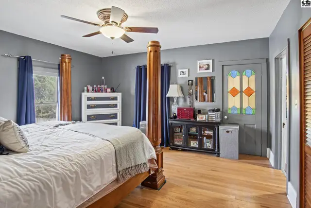 Spacious bedroom with a four-poster bed, hardwood floors, and decorative stained glass.