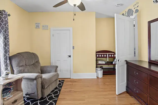 This room features light yellow walls, a ceiling fan, and hardwood floors.