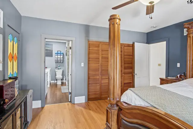 Spacious bedroom with wood floors, a ceiling fan, and a view into a full bathroom.