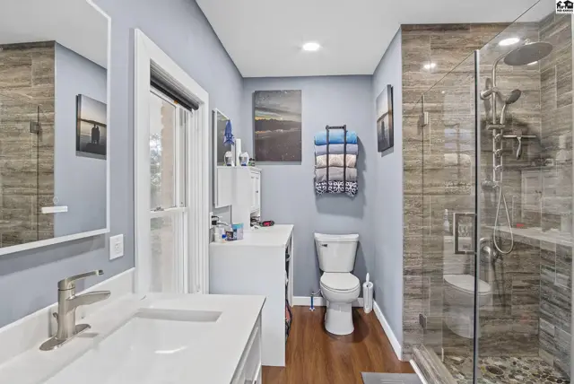 Modern bathroom features a double vanity, glass-enclosed shower with tiled walls, and wood-look flooring.