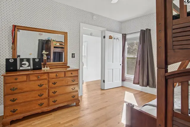 Wooden dresser with mirror sits on hardwood floors beneath patterned wallpaper.