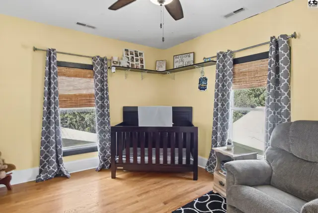 Corner room with yellow walls, wood floors, a crib, and patterned curtains.