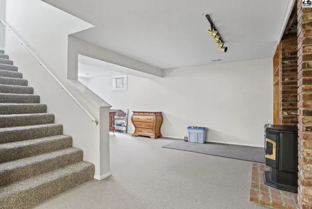 Finished basement with carpeted stairs, white walls, and a brick fireplace.