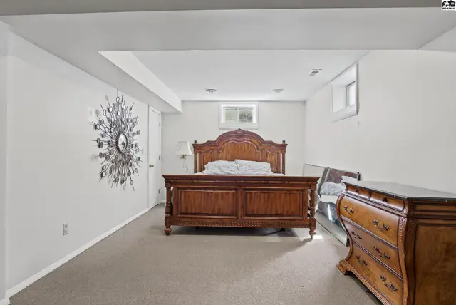 Spacious bedroom with a wooden bed frame and dresser on carpeted flooring.