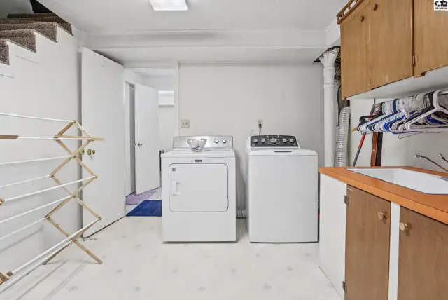 This laundry room features a washer, dryer, sink, and a folding drying rack.