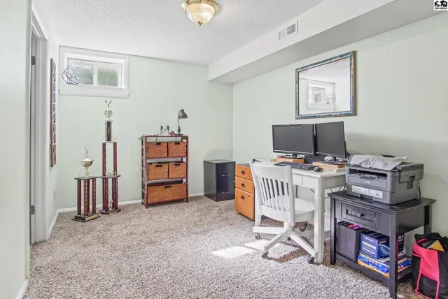 This room features carpeted floors, a desk with dual monitors, and a small window.