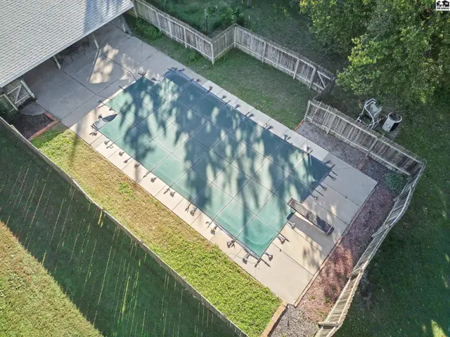 Rectangular swimming pool with a safety cover is surrounded by a concrete deck and wooden fence.