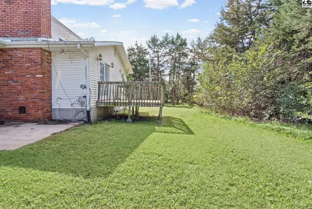 A wooden deck overlooks a grassy yard with mature trees.