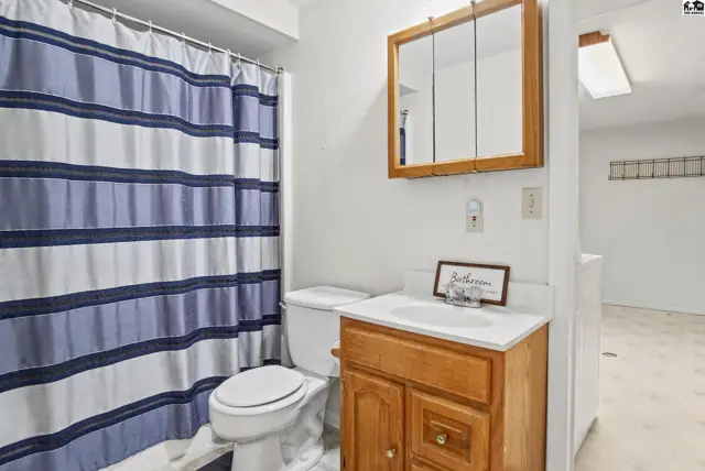 This bathroom features a vanity, toilet, and shower with a blue and white striped curtain.