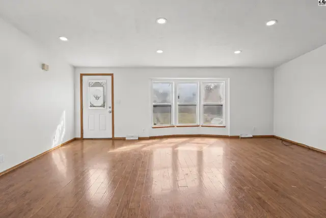 Spacious living area with hardwood floors and a large bay window.