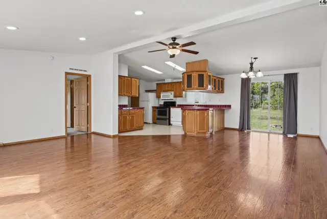 Spacious living area with wood flooring opens to a kitchen with oak cabinets.