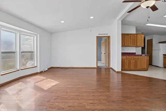 Spacious living area with wood flooring, large windows, and an adjacent kitchen with wood cabinetry.