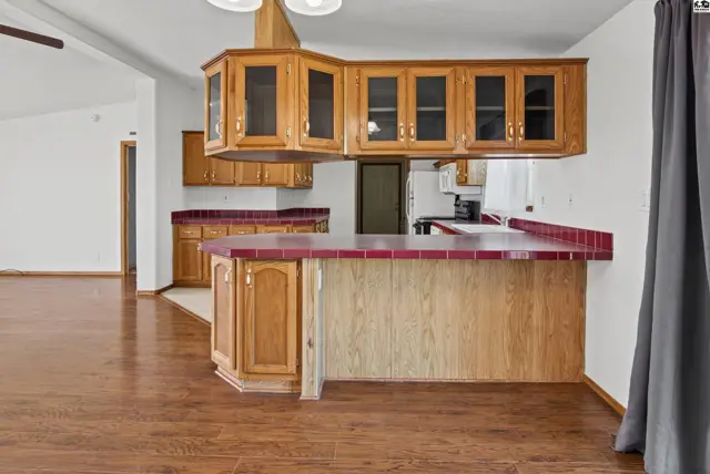 This kitchen features wood cabinetry, a breakfast bar with tile countertops, and wood flooring.