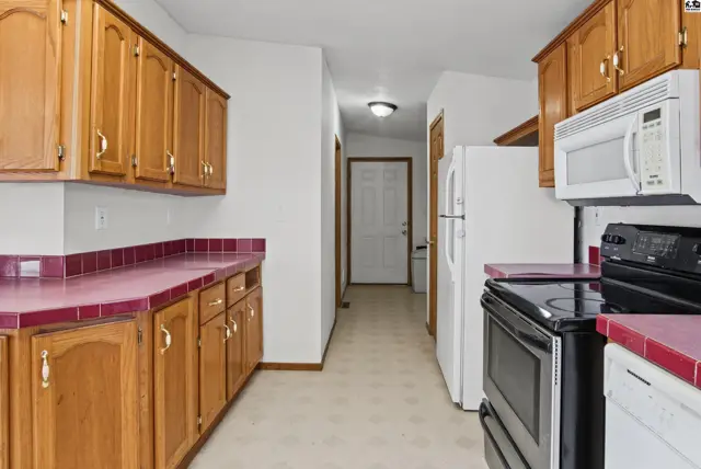 This kitchen features wood cabinetry, white appliances, and red countertops.