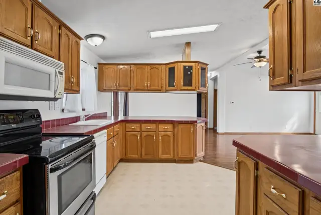 Spacious kitchen features wood cabinetry, white appliances, and a double sink.