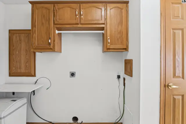 This laundry room features oak cabinetry, a white washer, and a wood-paneled door.