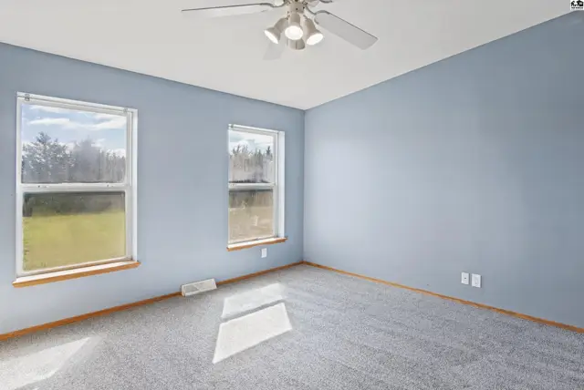 This room features light blue walls, grey carpet, and two large windows.