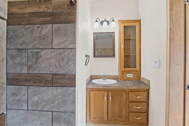 This bathroom features a wood vanity, stone tile accent wall, and a glass-front medicine cabinet.