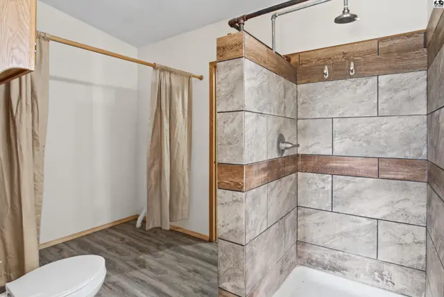 This bathroom features a tiled shower stall, a toilet, and a closet with curtains.