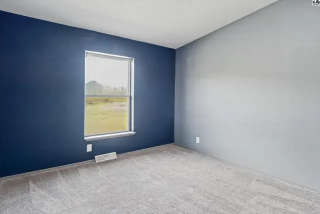 This room features a large window, carpeted floor, and two-tone painted walls.