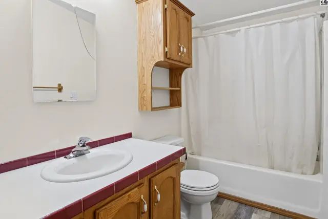This bathroom features a vanity with a white sink, a wooden cabinet, and a bathtub with a shower curtain.