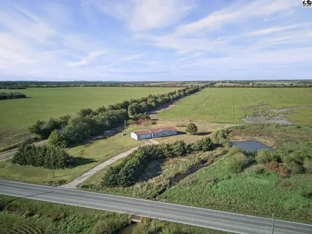 This property features a white building with a red roof surrounded by fields and trees.